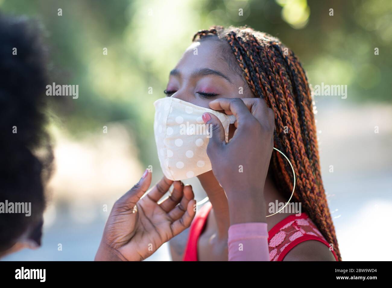 Belle fille afro-américaine aide son ami à mettre un masque facial sur. Le revêtement de visage est important pour protéger contre les virus, y compris COVID-19 Banque D'Images