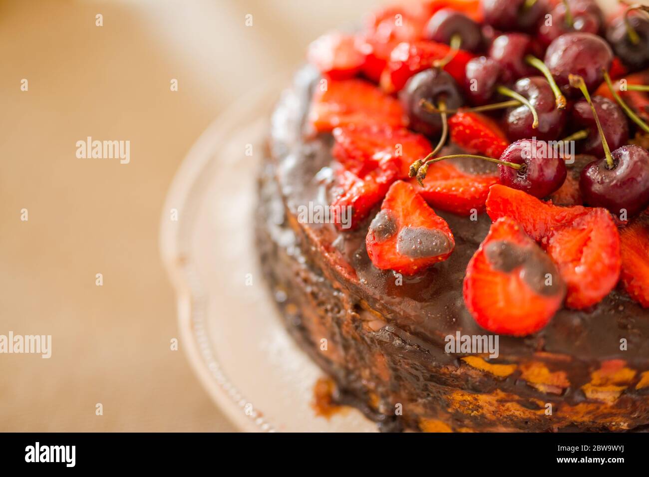 Gâteau au chocolat maison traditionnel dessert sucré avec glaçage brun, cerises, framboise, cassis sur fond de bois vintage. Photo de nourriture sombre Banque D'Images