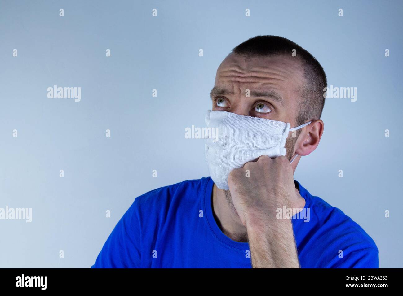 Jeune homme dans un masque de protection sur fond bleu. Pense, rêve, met sa main sur son menton. copyspace pour le texte. Banque D'Images