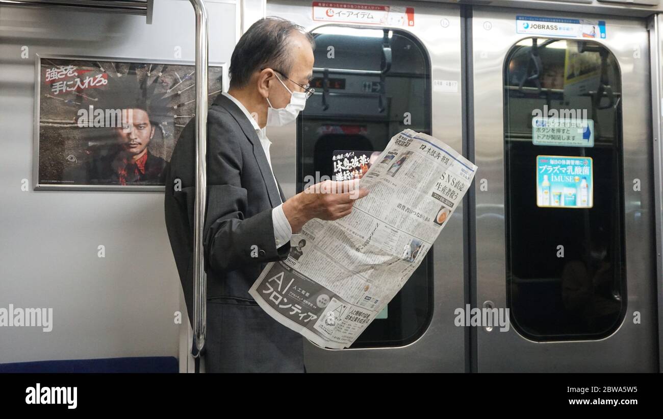 Tokyo, Japon : vieil homme japonais portant un masque lisant dans un train Banque D'Images