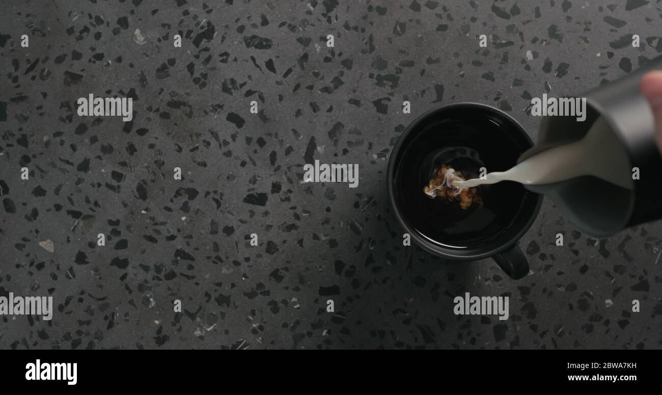 verser la crème dans le café noir dans une tasse noire sur le béton vue de dessus de l'arrière-plan Banque D'Images