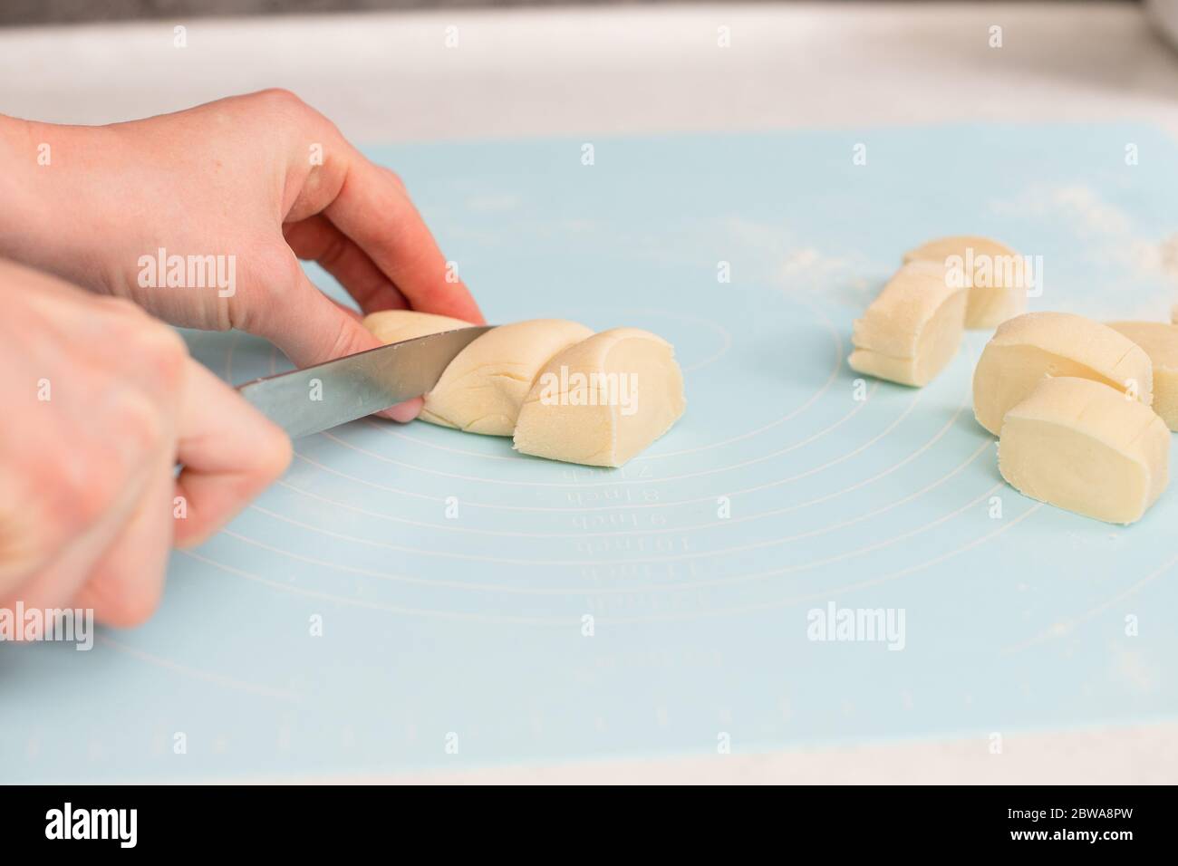 Couteau à main femelle et découpe de petits morceaux de pâte à pain sur une feuille de tapis en silicone bleu, pâtisserie maison Banque D'Images