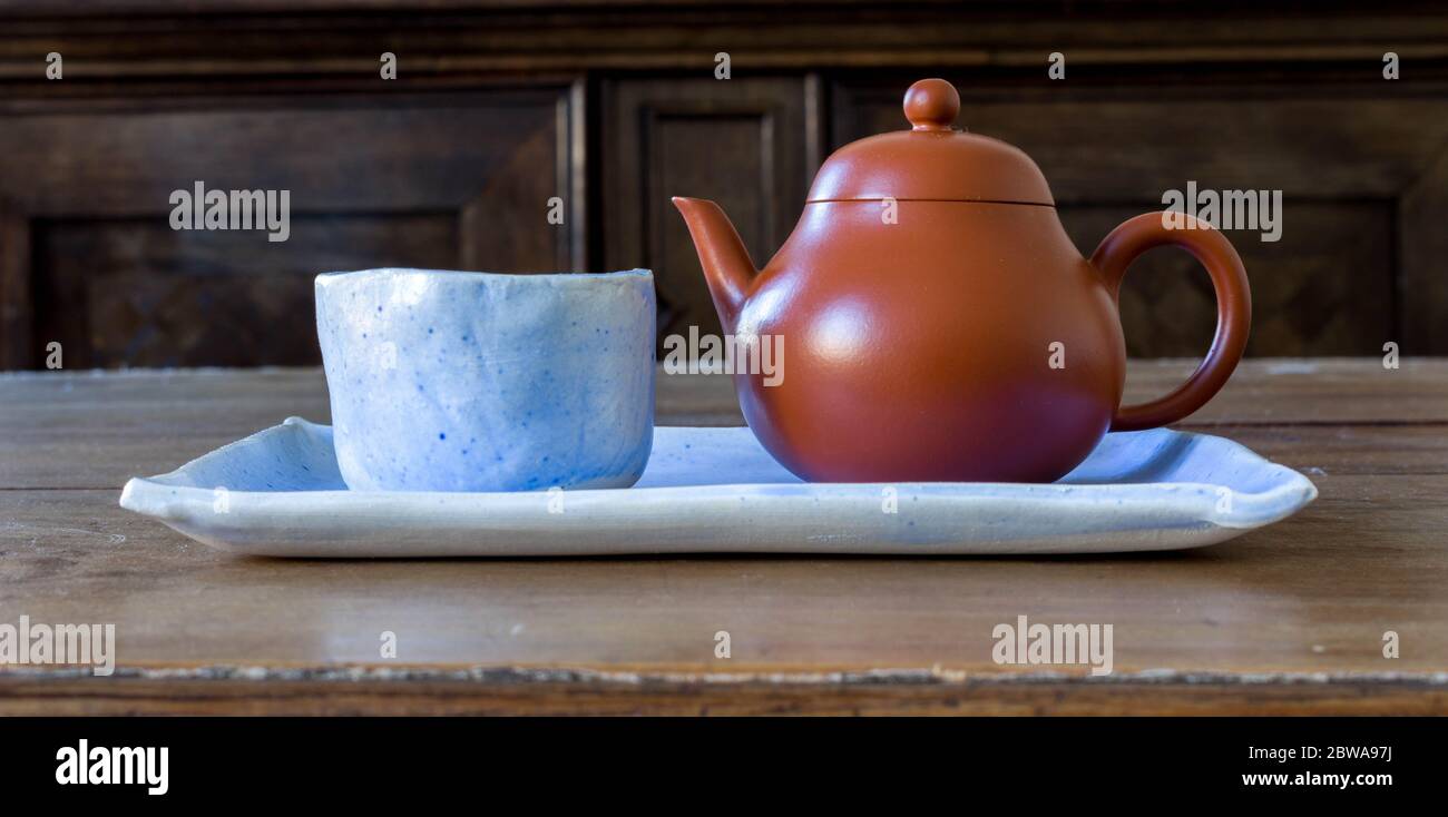 Petit gobelet en céramique bleu clair fait main avec une petite théière brune sur une plaque en céramique bleu clair et une table en bois. Véritable culture chinoise du thé vert Banque D'Images