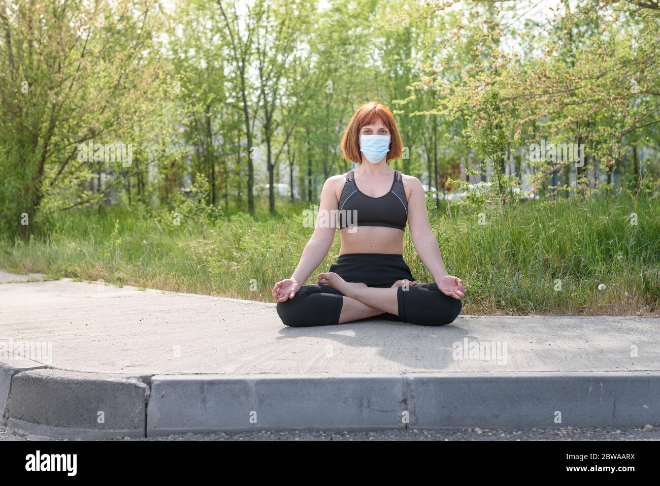 Fille en position lotus avec masque sirurgical dans fond de nature. Concept de coronavirus Banque D'Images