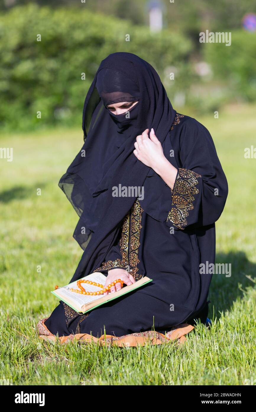 La femme islamique exécute la prière du matin assis sur l'herbe verte un parc. Banque D'Images