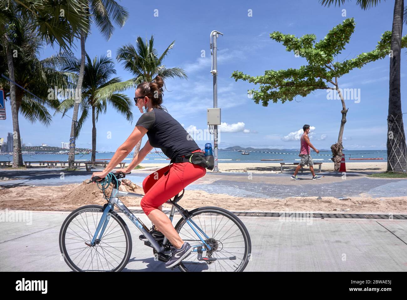 Exercice Covid 19. Femme prenant l'exercice de vélo pendant le verrouillage du coronavirus avec l'homme marchant dans l'arrière-plan. Thaïlande, Asie Banque D'Images