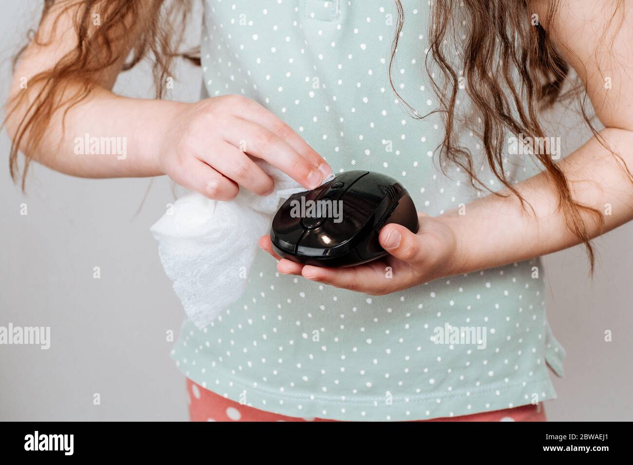 Une fille essuye une souris d'ordinateur avec un chiffon désinfectant. Concept de désinfection des surfaces à partir de bactéries ou de virus Banque D'Images