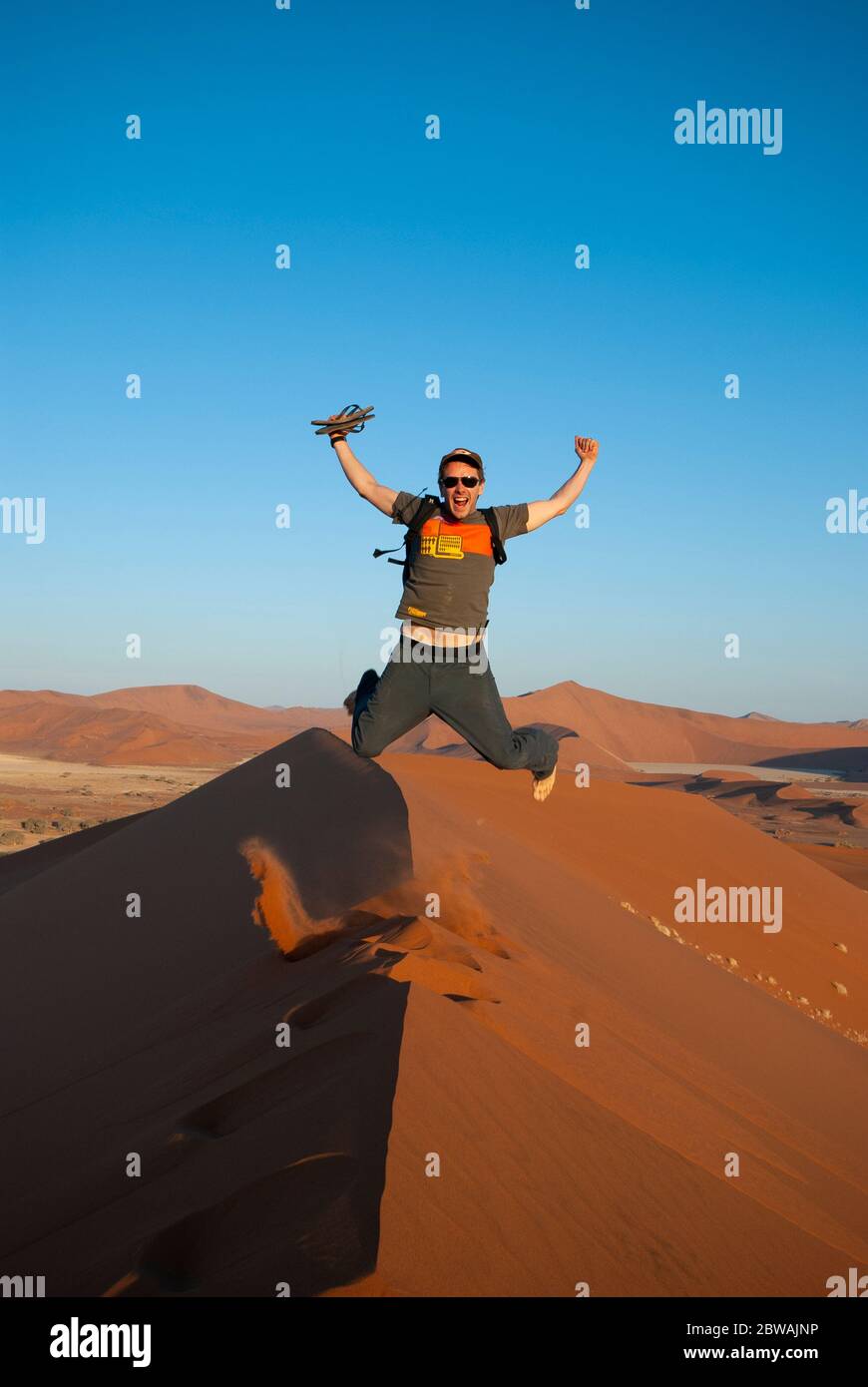 Un jeune homme heureux sautant au sommet d'une dune de sable dans le désert du Namib près de Sousssusvlei en Namibie, en Afrique Banque D'Images