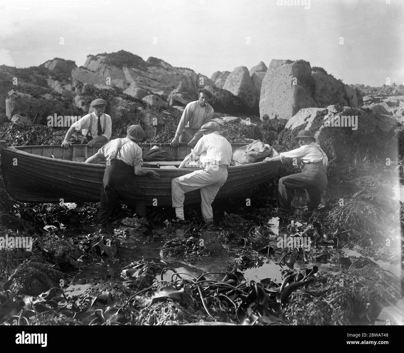 Les insulaires du chenal essaient de se délotter de leur bateau sur le rivage rocheux après avoir rassemblé des ormes ou des ormeaux . 8 octobre 1920 Banque D'Images