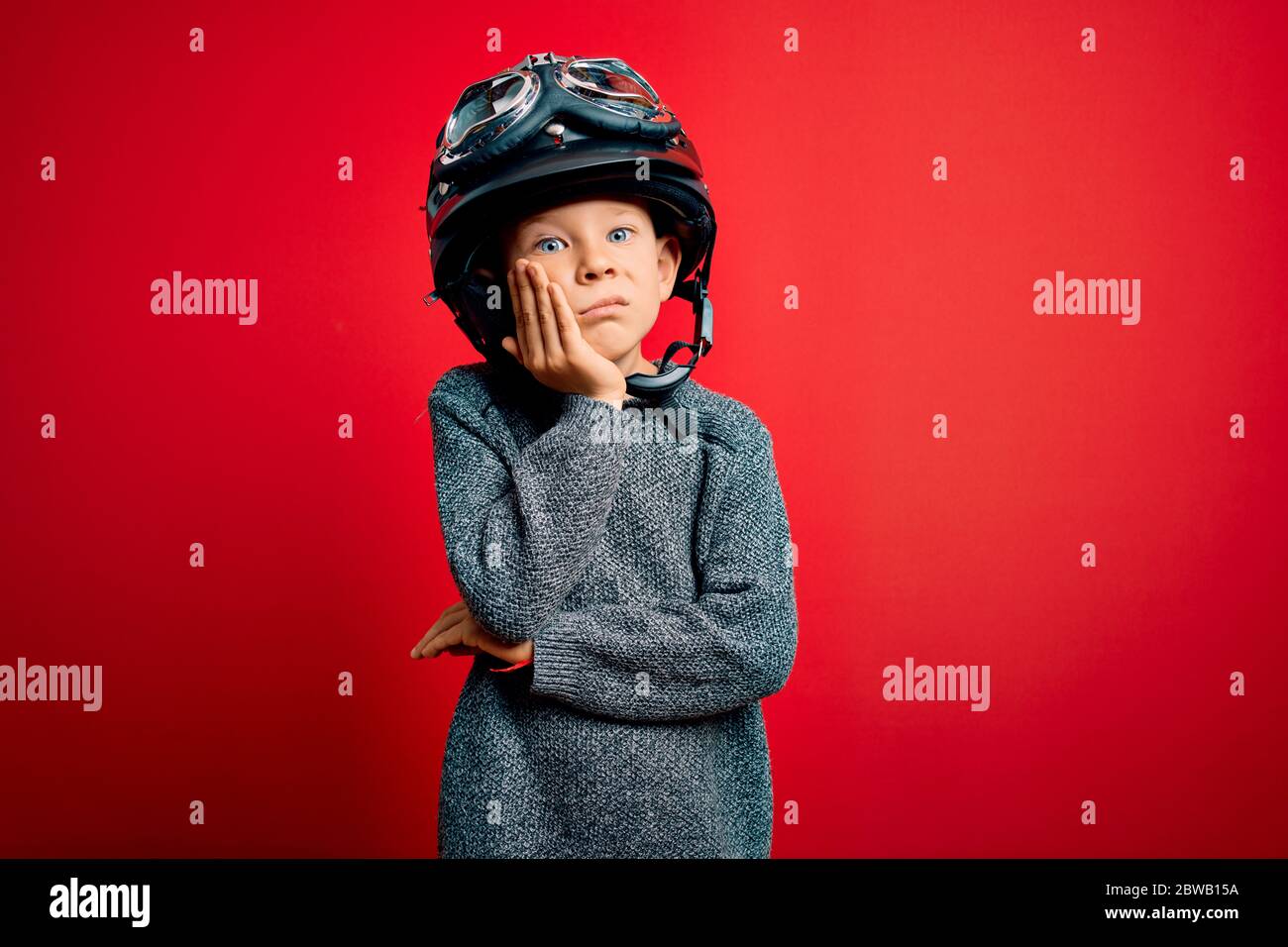 Jeune petit casien enfant portant un casque moto vintage de motard et des  googles sur fond rouge penser à l'aspect fatigué et ennuyé avec la  dépression pr Photo Stock - Alamy