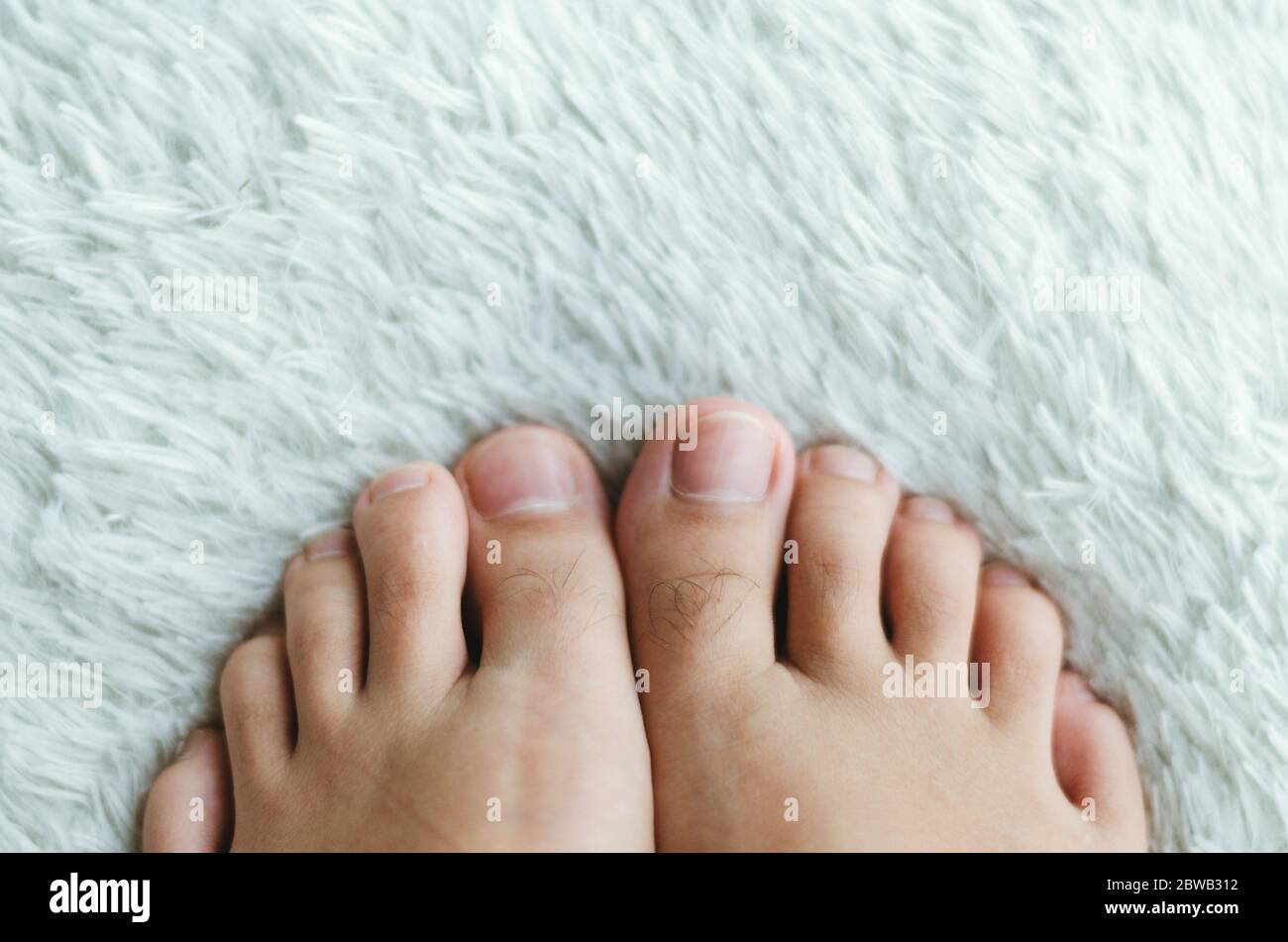 Orteils poilus avec des ongles pour faire marcher dans un tapis blanc fourrure. Banque D'Images