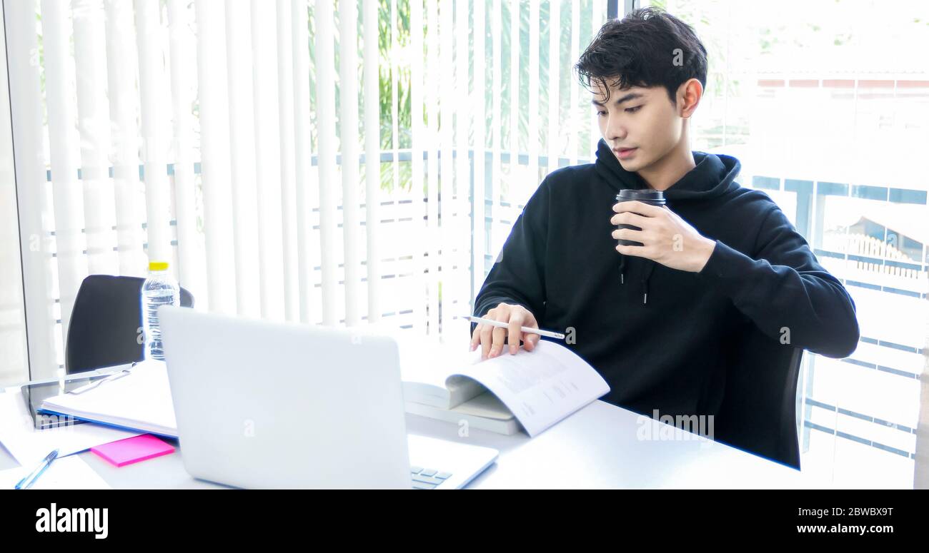 Les étudiants asiatiques lisent des livres et utilisent un ordinateur portable pour trouver des informations pour le travail et les études en ligne. Banque D'Images