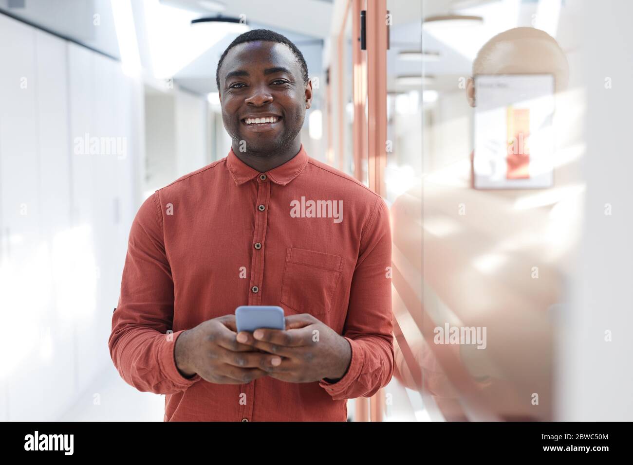 Portrait de l'homme afro-américain contemporain tenant un smartphone et souriant devant l'appareil photo, debout dans un bureau futuriste, Copy spa Banque D'Images