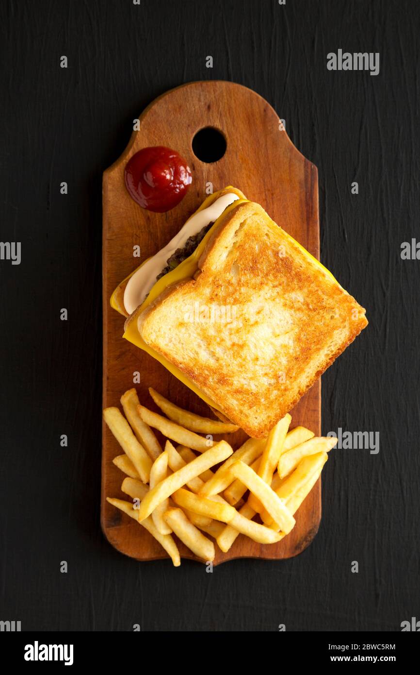 Hamburger au fromage frais grillé et frites sur un panneau de bois rustique sur fond noir, vue du dessus. Pose à plat, en hauteur, par le dessus. Banque D'Images