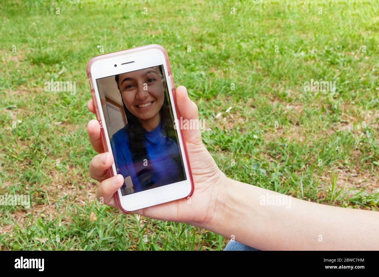 Gros plan d'un smartphone lors d'un appel vidéo avec une jeune fille souriante. Photo prise à l'extérieur sur une pelouse verte au printemps. Banque D'Images