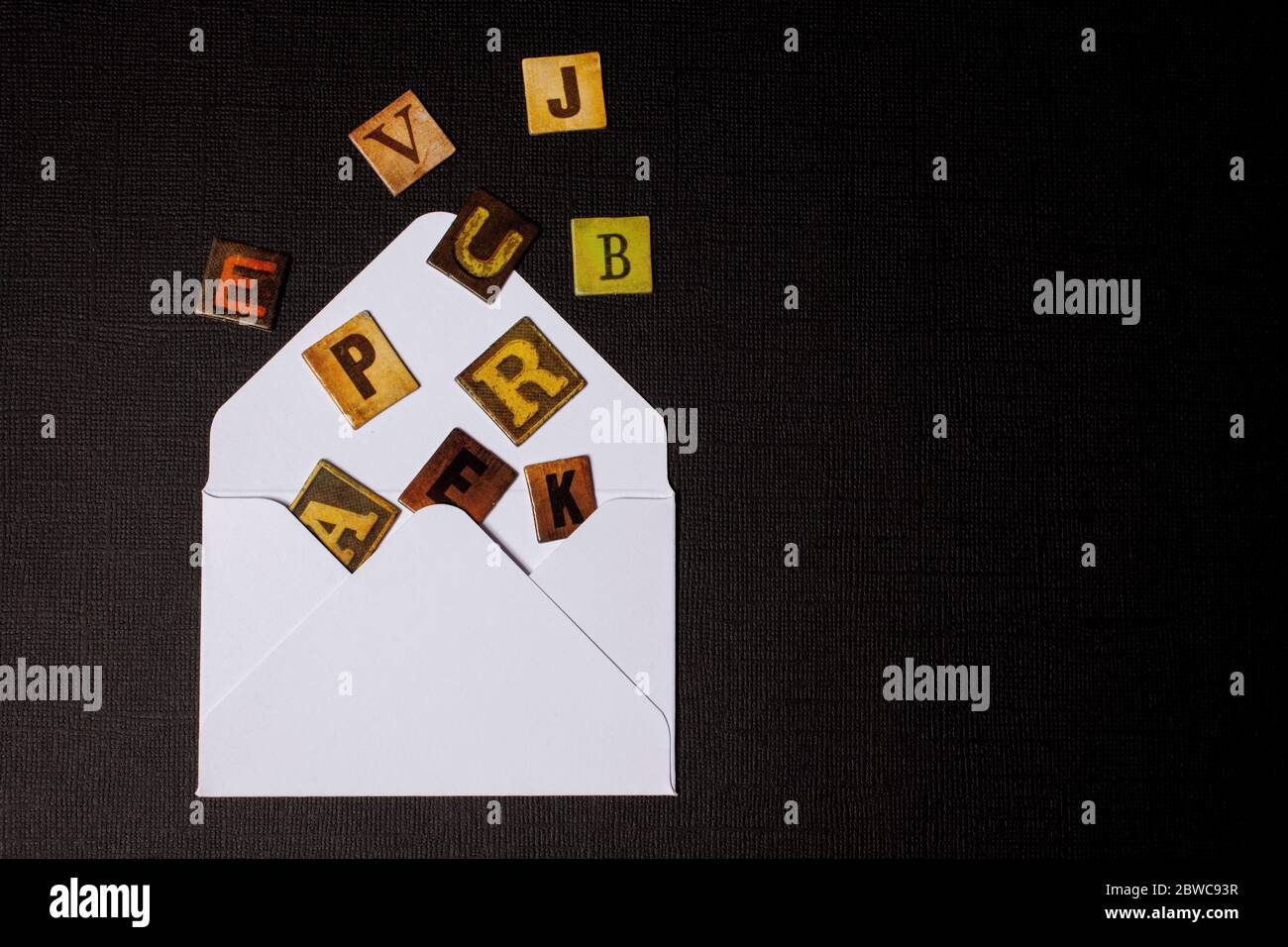 Texte, message, lettres dispersés dans une enveloppe blanche isolée sur fond noir Banque D'Images