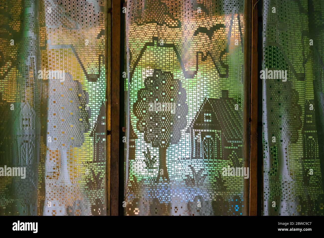 Rideaux transparents d'époque blanc ajouré avec maisons, arbres, plantes, fleurs, oiseaux, motif de nuages devant la lumière sur l'ancienne fenêtre en bois Banque D'Images
