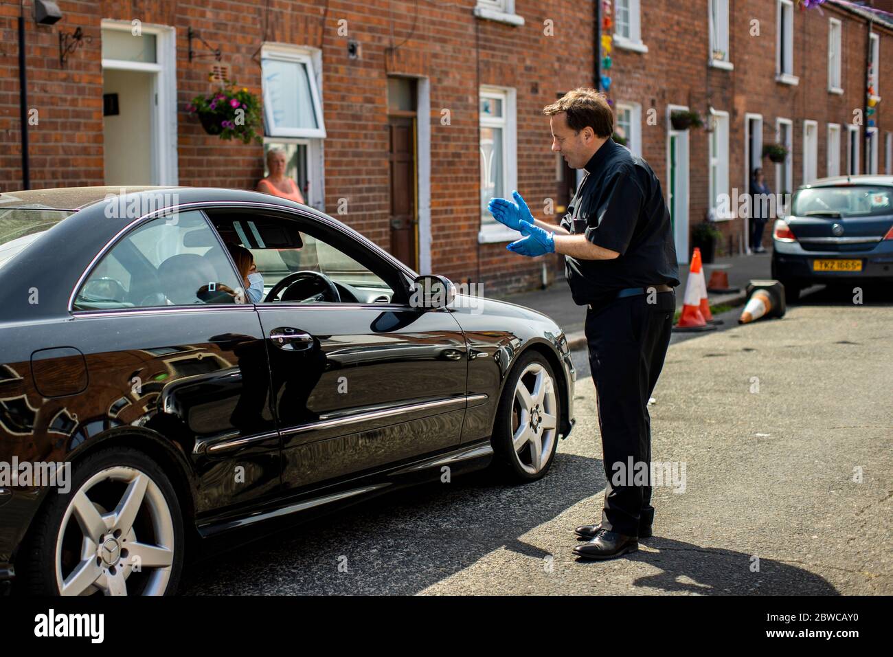 Le FR Tim Bartlett de l'église St Mary à Belfast offre une bénédiction à une femme dans sa voiture sur John Street pendant le dimanche de la Pentecôte. Les paroissiens ont demandé à l'église de visiter la communauté locale pour livrer l'eau Sainte pendant le confinement. Banque D'Images