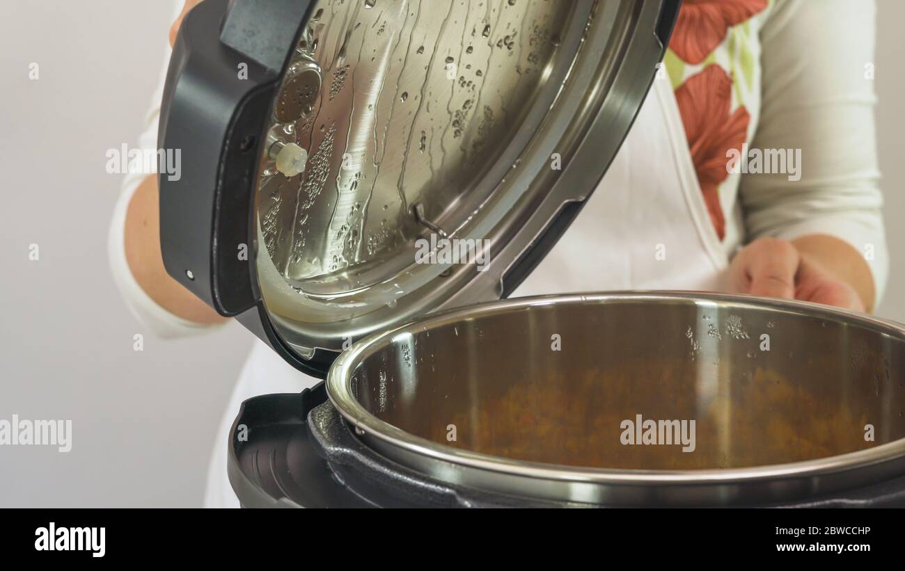 Femme soulevant le couvercle de la cuisinière multiple. Cuisiner de la soupe dans une cuisinière électrique moderne Banque D'Images