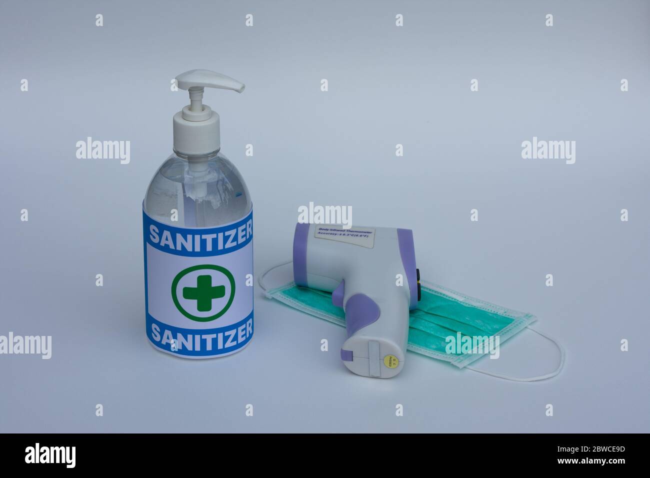 Flacon de gel nettoyant pour alcool, thermomètre infrarouge sans contact et masques chirurgicaux sur fond blanc. Banque D'Images