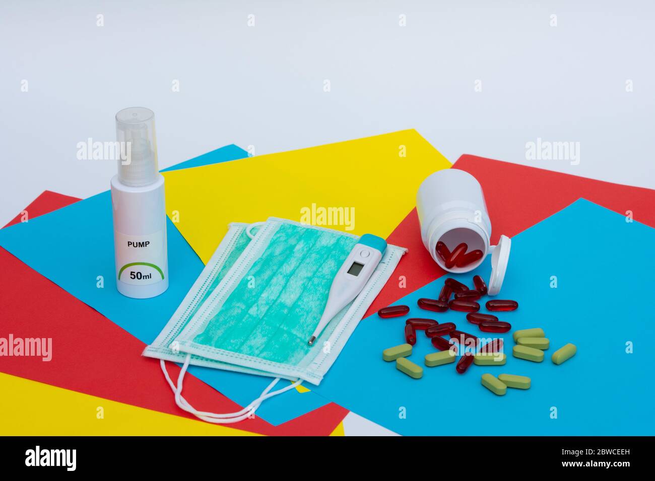 Gel désinfectant pour les mains, masque chirurgical, thermomètre électronique numérique et pilules sur fond multicolore. Banque D'Images
