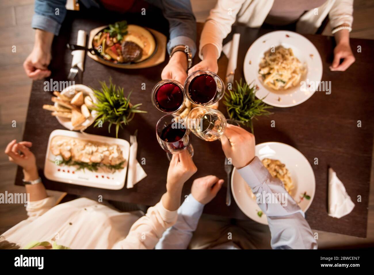 Quatre mains avec du vin rouge sur la table servie avec des plats au restaurant Banque D'Images