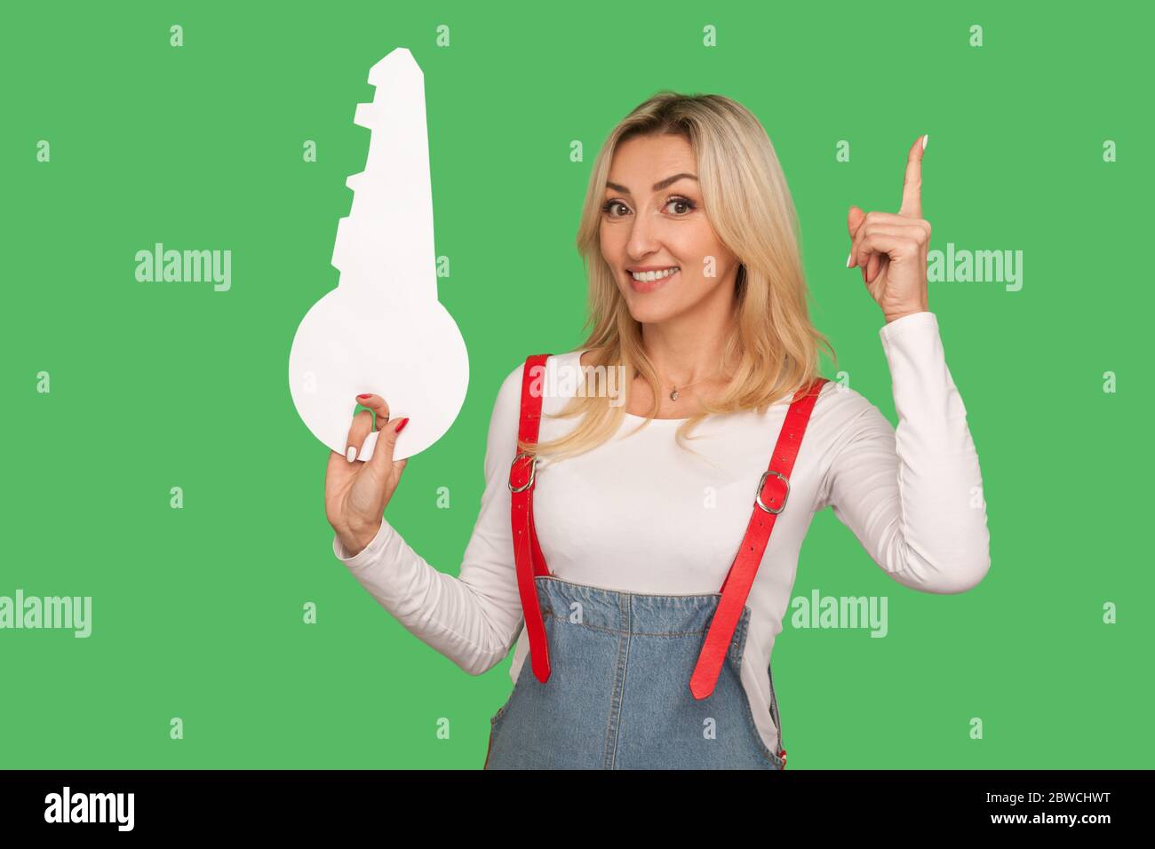 Excellente idée. Portrait d'une femme blonde adulte inspirée dans une combinaison élégante en denim montrant et tenant la clé comme la solution intelligente de génie. ind Banque D'Images