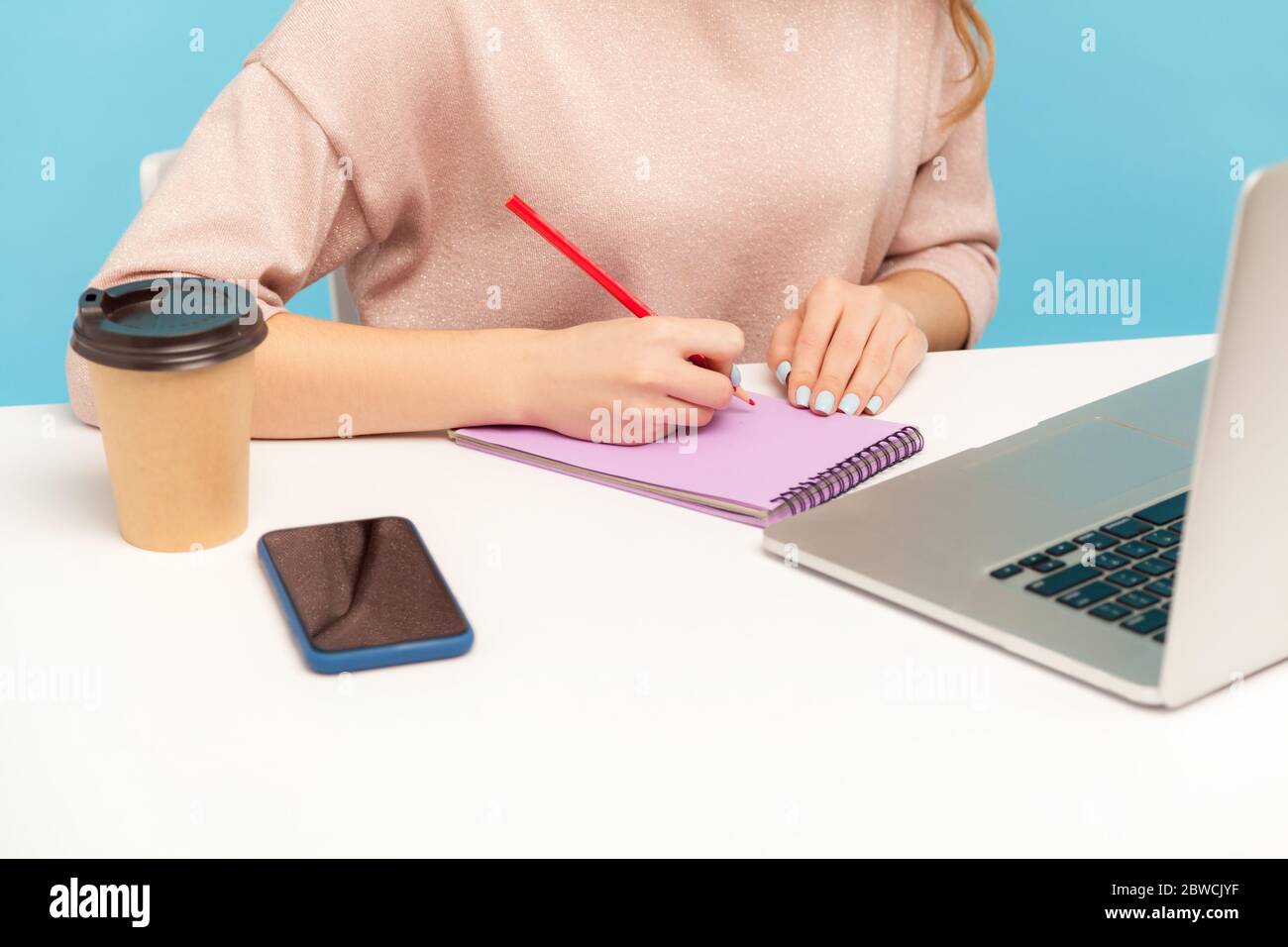 Gros plan de la journaliste féminine prenant des notes avec un crayon sur le papier cahier et travaillant sur ordinateur portable, étudiant étudiant, écrire liste à faire, correspondance. i Banque D'Images