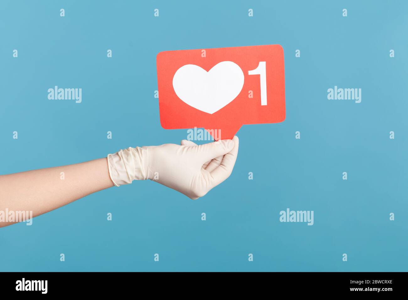 Vue latérale du profil gros plan de la main humaine en gants chirurgicaux blancs tenant les médias sociaux comme le bâton. En intérieur, prise de vue en studio, isolée sur fond bleu. Banque D'Images
