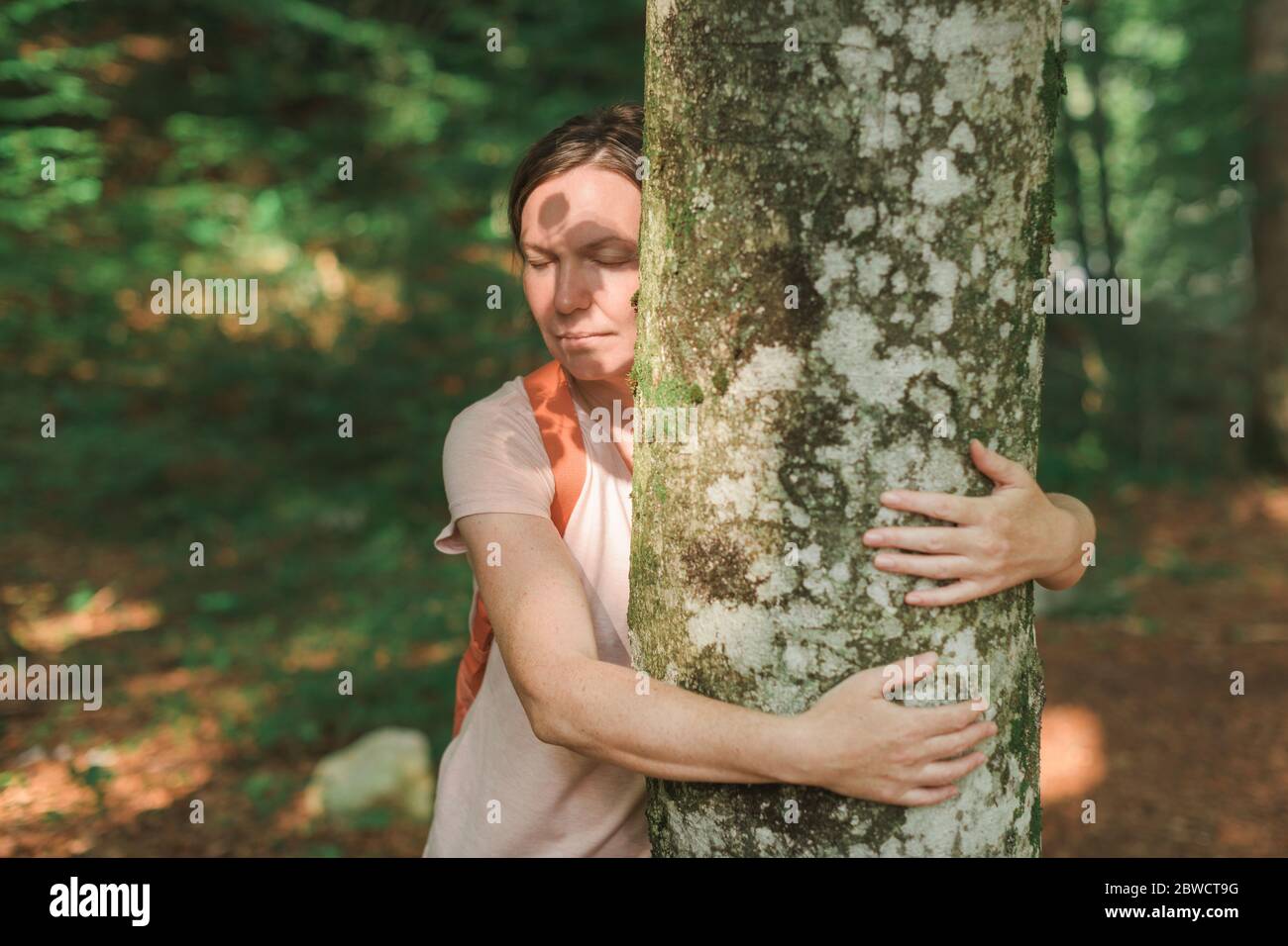 Femme embrasse le tronc d'arbre dans la forêt, femme écologiste avec ses bras autour de l'arbre, foyer sélectif Banque D'Images