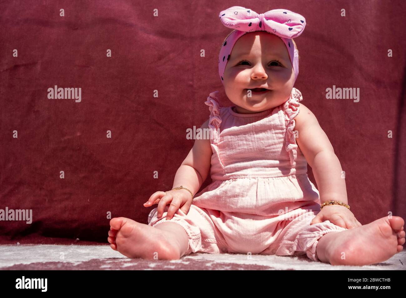 Mignon petite fille de porter chapeau et s'asseoir sur la moquette à l'extérieur, regardant l'appareil photo et sourire Banque D'Images