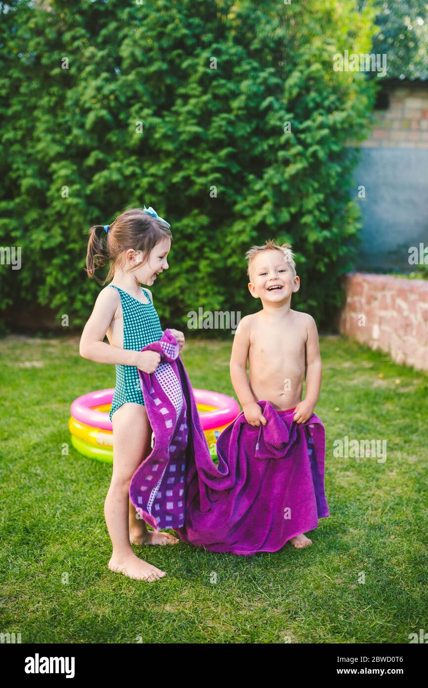 Les enfants du Caucase sont heureux de jouer, enveloppés dans une grande  serviette de plage d'été dans la chaleur après avoir nagé dans une piscine  gonflable ronde. Les enfants s'échauffent Photo Stock -
