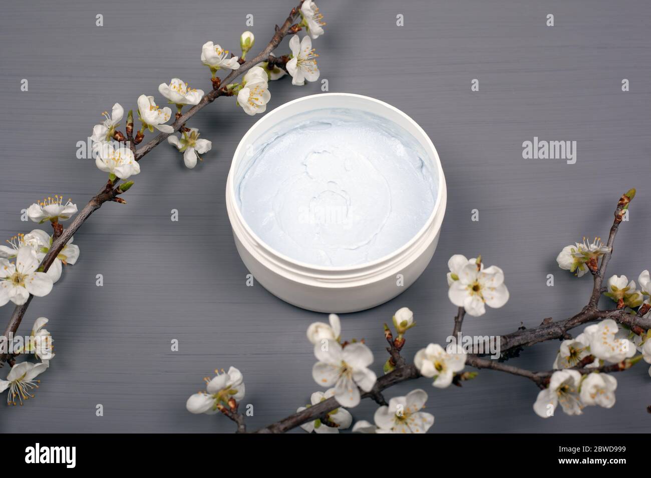 gommage blanc à corps rond avec branches de fleurs blanches de cerise sur fond gris gros plan, cosmétiques nettoyants soins de la peau. Banque D'Images