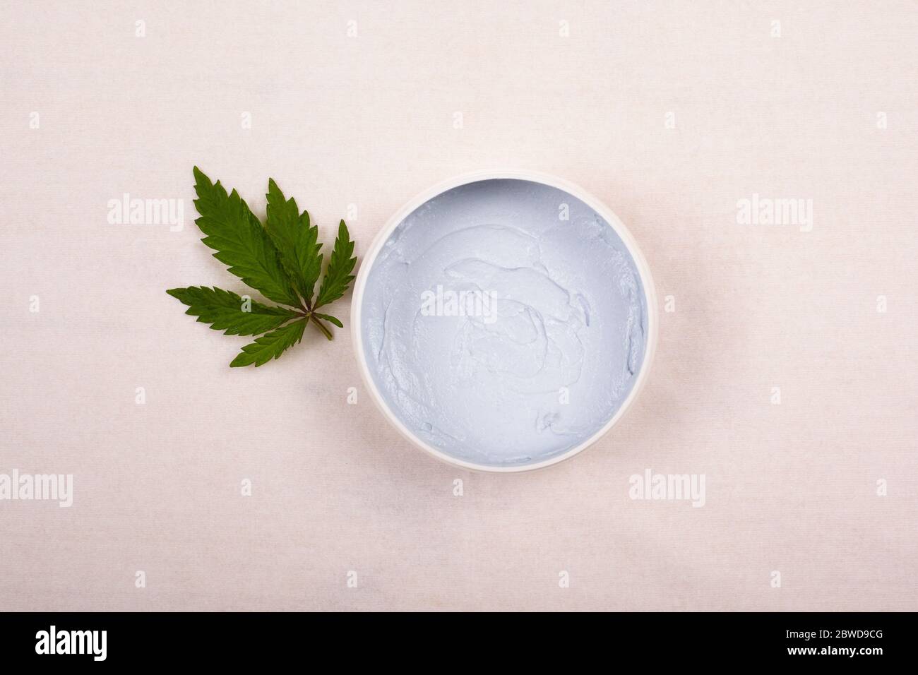 pot rond blanc avec un gommage corporel avec une feuille de marijuana sur un fond blanc vue du dessus, cosmétiques, soins de la peau, beauté. Banque D'Images