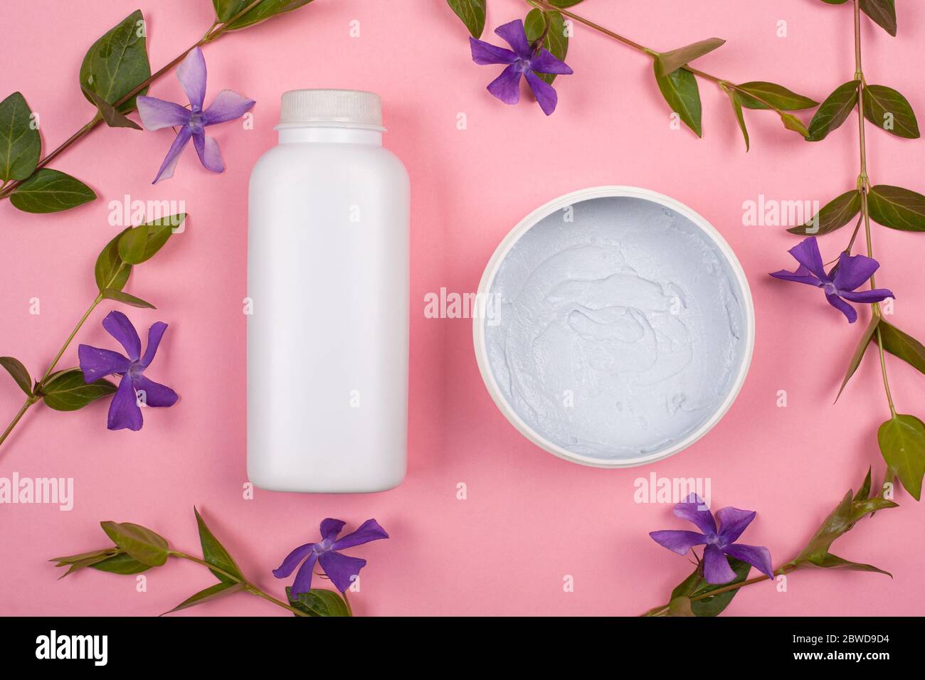 bouteilles blanches avec cosmétiques pour le corps sur fond rose avec branches de fleurs sauvages violettes vue du dessus. soins de la peau, beauté. Banque D'Images