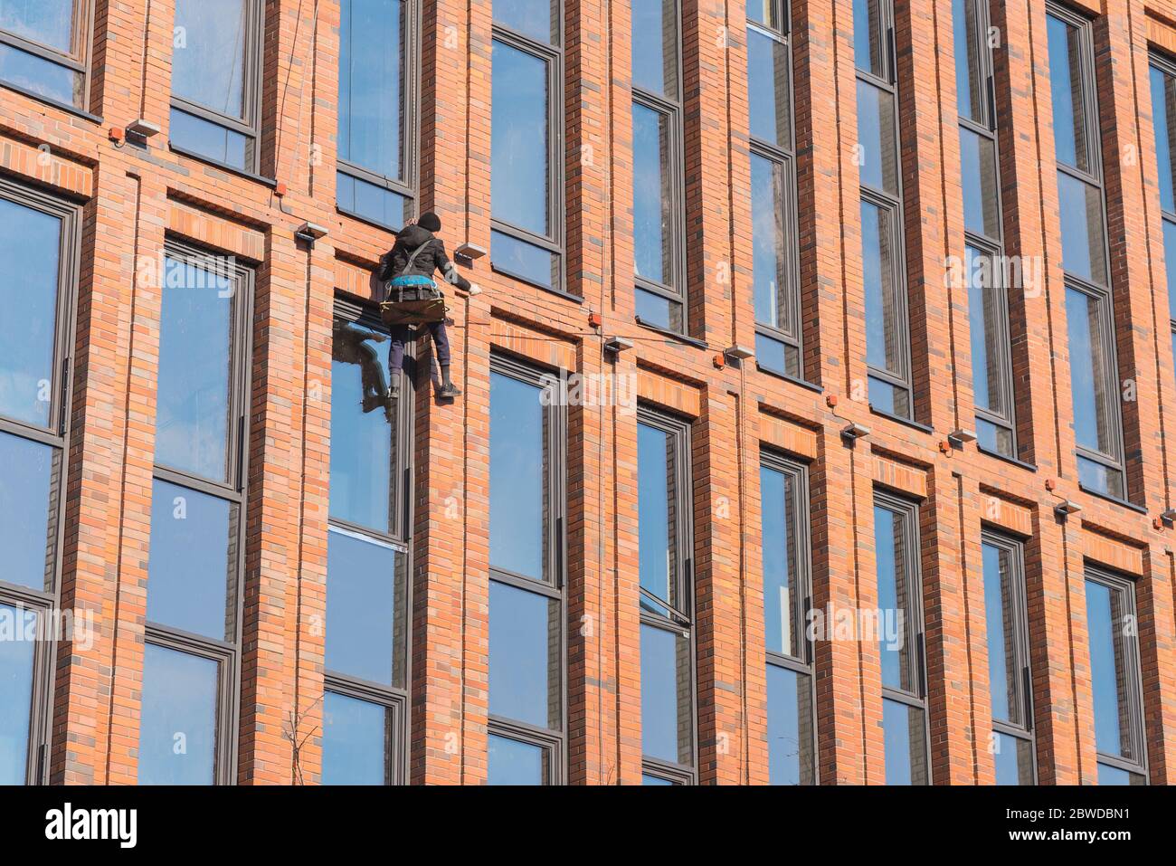 Un technicien d'accès à la corde travaille sur la façade du bâtiment en hauteur. Banque D'Images