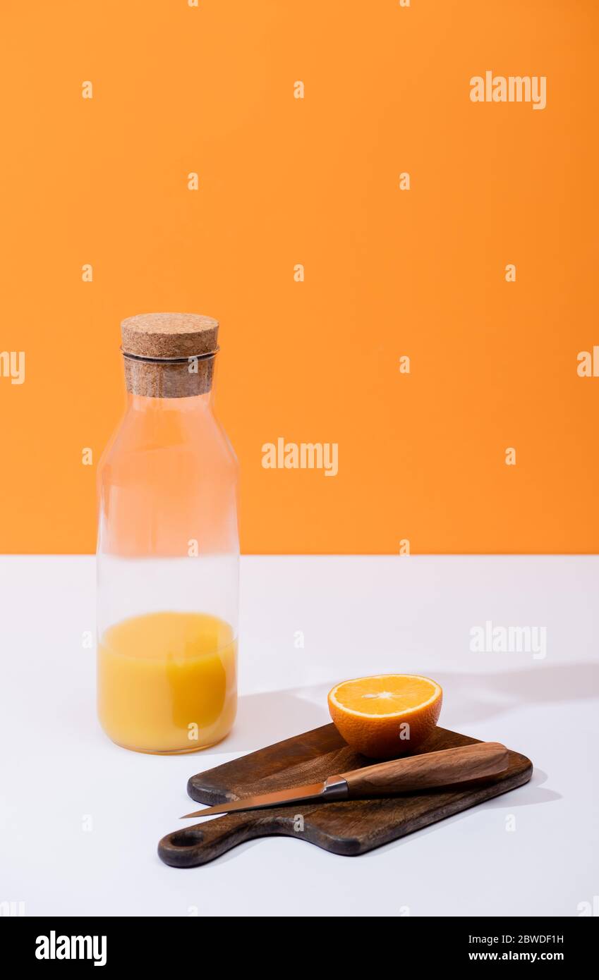 jus d'orange frais en bouteille de verre près des fruits coupés sur une planche à découper en bois avec couteau sur surface blanche isolée sur l'orange Banque D'Images