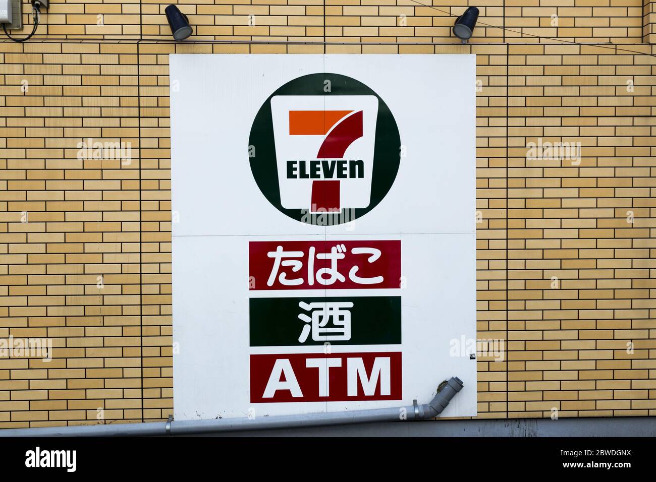 7-Eleven Convenience Store signe contre le mur de brique jaune à Tokyo, Japon avec des lettres japonaises qui lisent "sept onze" et "ATM" Banque D'Images
