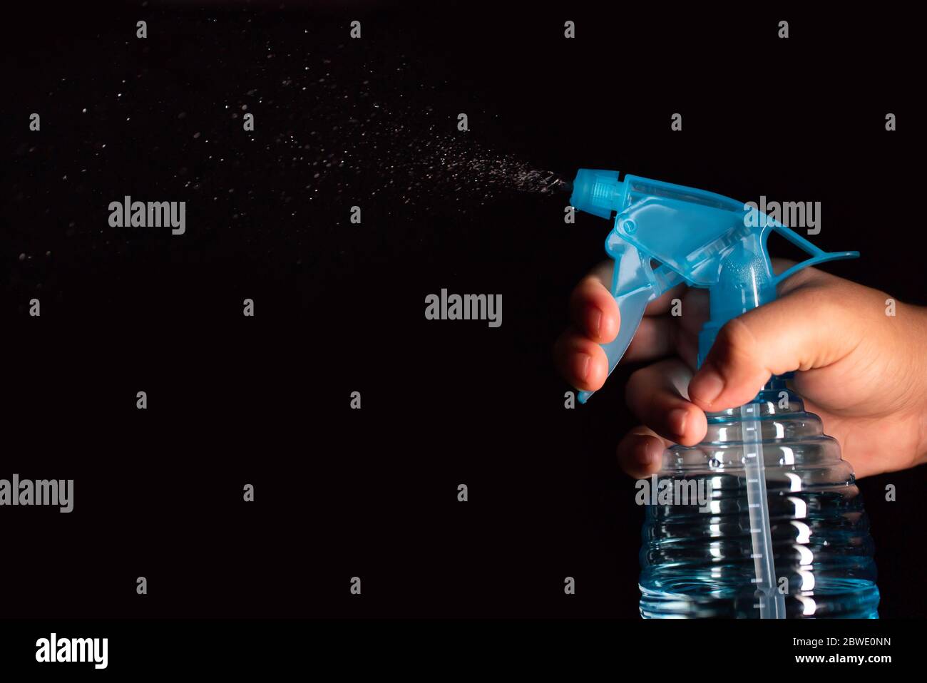 Une main de fille vaporisant un spray bleu avec un produit de nettoyage à fond noir Banque D'Images