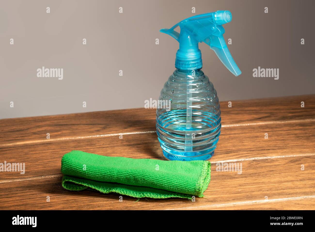 Une serviette en microfibre avec un pulvérisateur de nettoyage bleu sur un panneau en bois et un fond blanc Banque D'Images