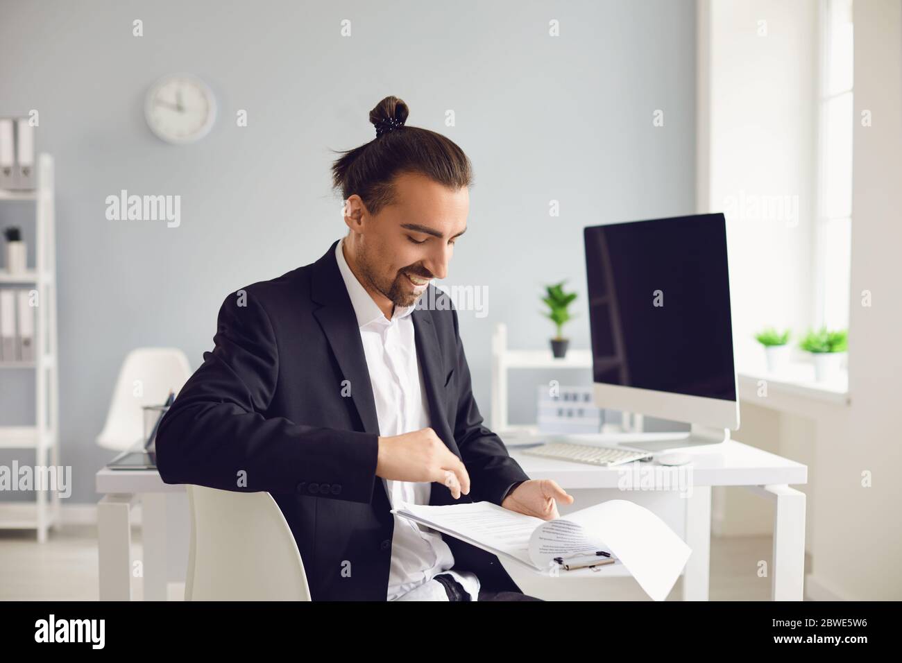 Un homme brunette dans une veste noire assise à la table travaille avec des papiers au bureau. Banque D'Images