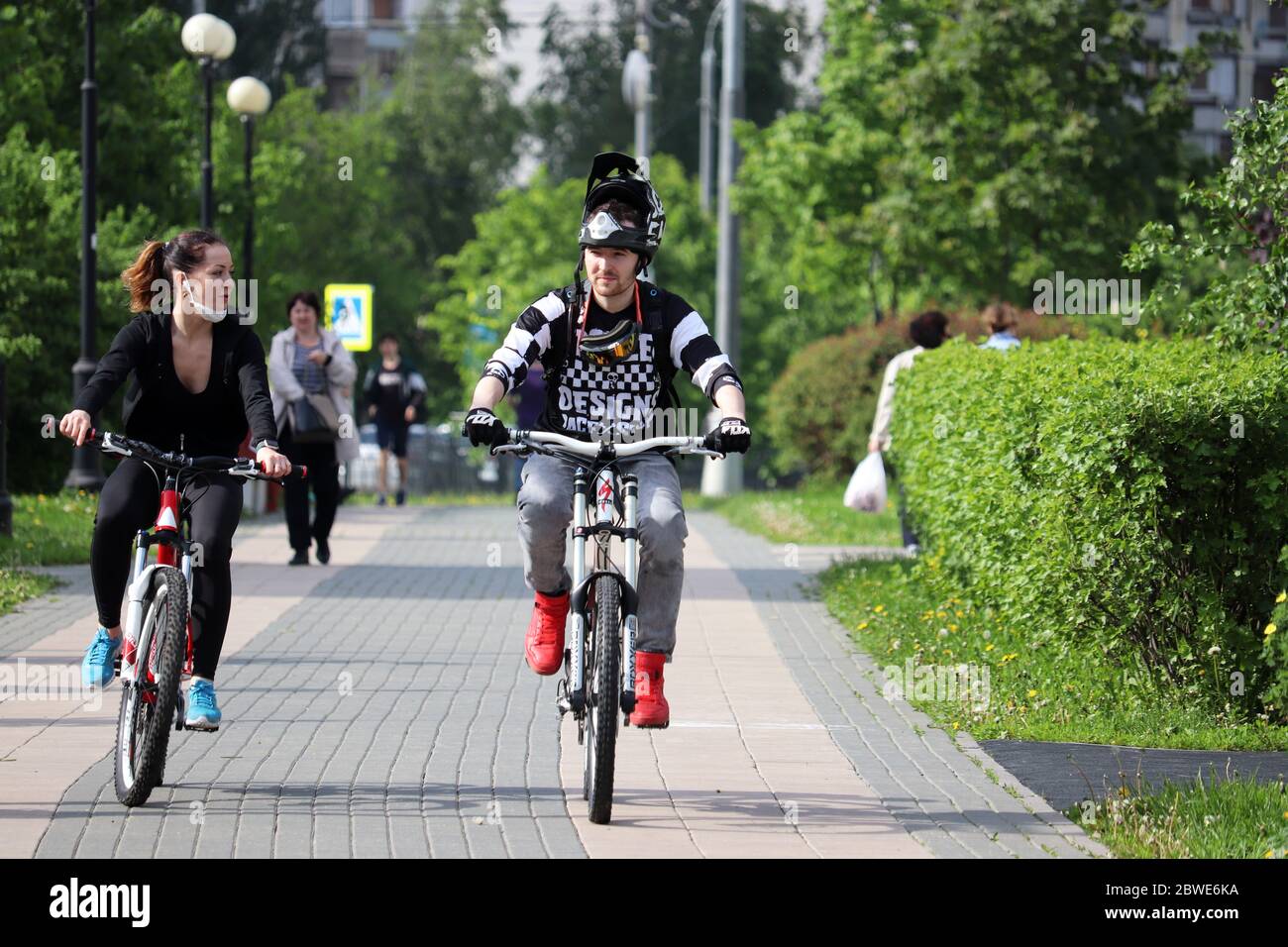 Un couple heureux fait du vélo dans un parc vert sur fond de personnes à pied. Concept de cyclisme, loisirs en famille, Journée mondiale du vélo Banque D'Images