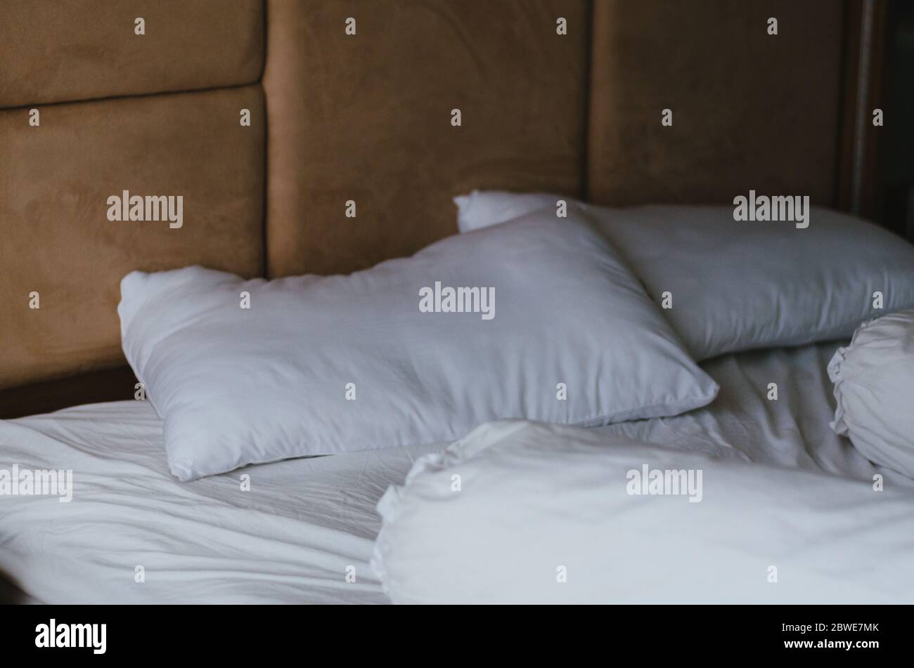 Un lit désordonné avec deux oreillers et deux oreillers et draps en coton, tous en blanc, avec un fond beige derrière le lit. Banque D'Images