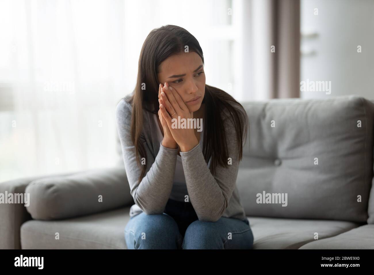 Une jeune femme attentionnés et contrariée assise sur un canapé à la maison Banque D'Images