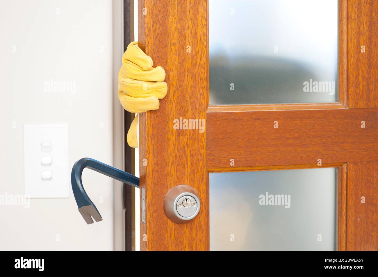 Cambrioleur, voleur avec des gants, tenant le crowbar se brisant dans la maison, déverrouillez la porte, silhouette visible floue derrière des fenêtres laiteuses, avec espace de copie. Banque D'Images