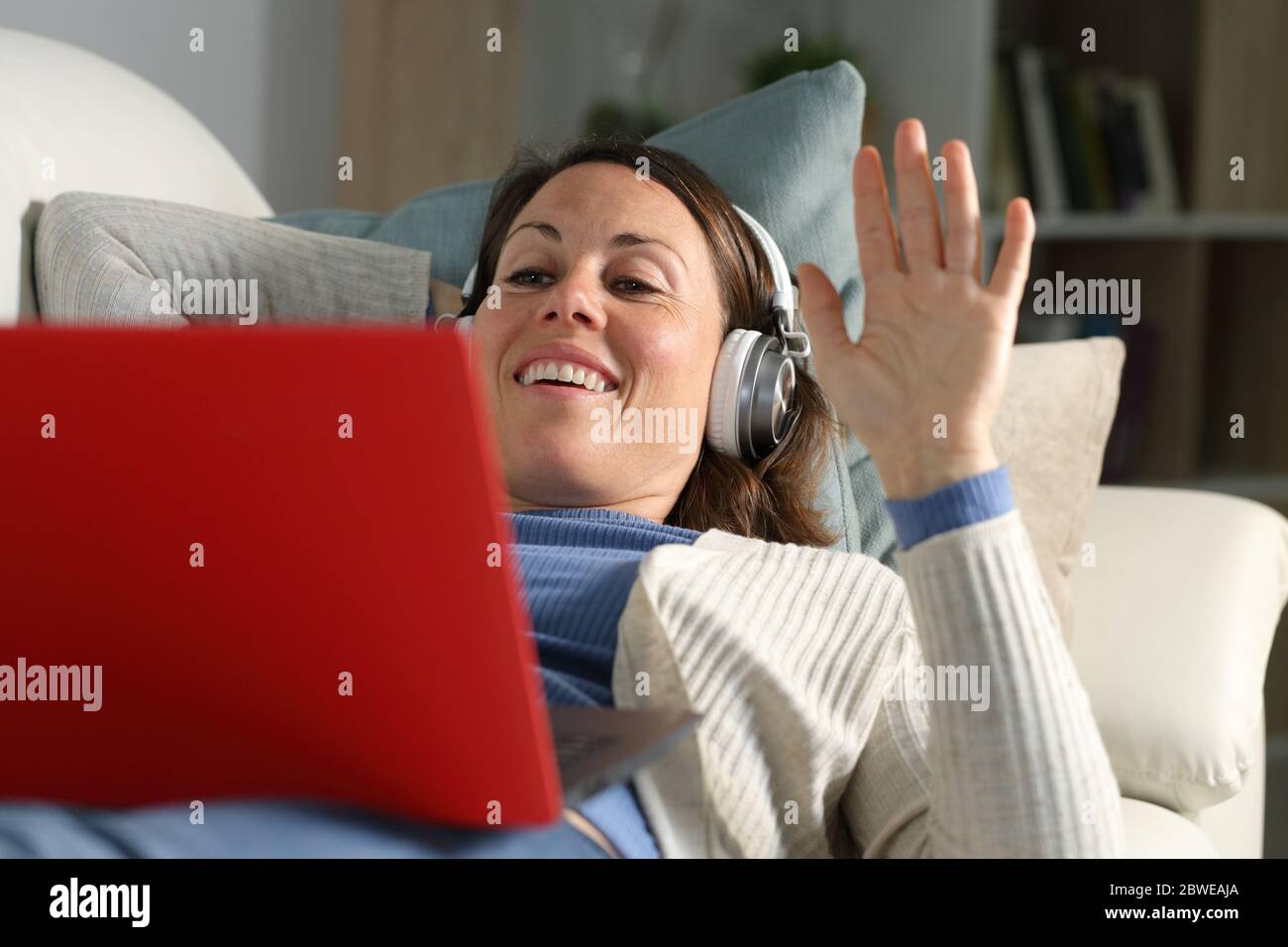 Bonne femme adulte, filant avec un casque, se faisant traîner sur un ordinateur portable posé sur un canapé dans le salon à la maison Banque D'Images