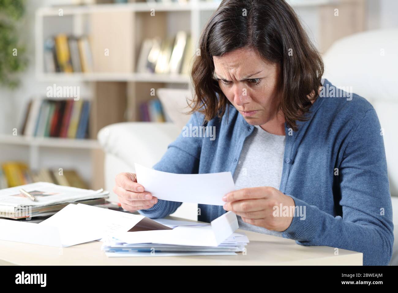 Femme adulte confuse regardant les reçus assis dans le salon à la maison Banque D'Images