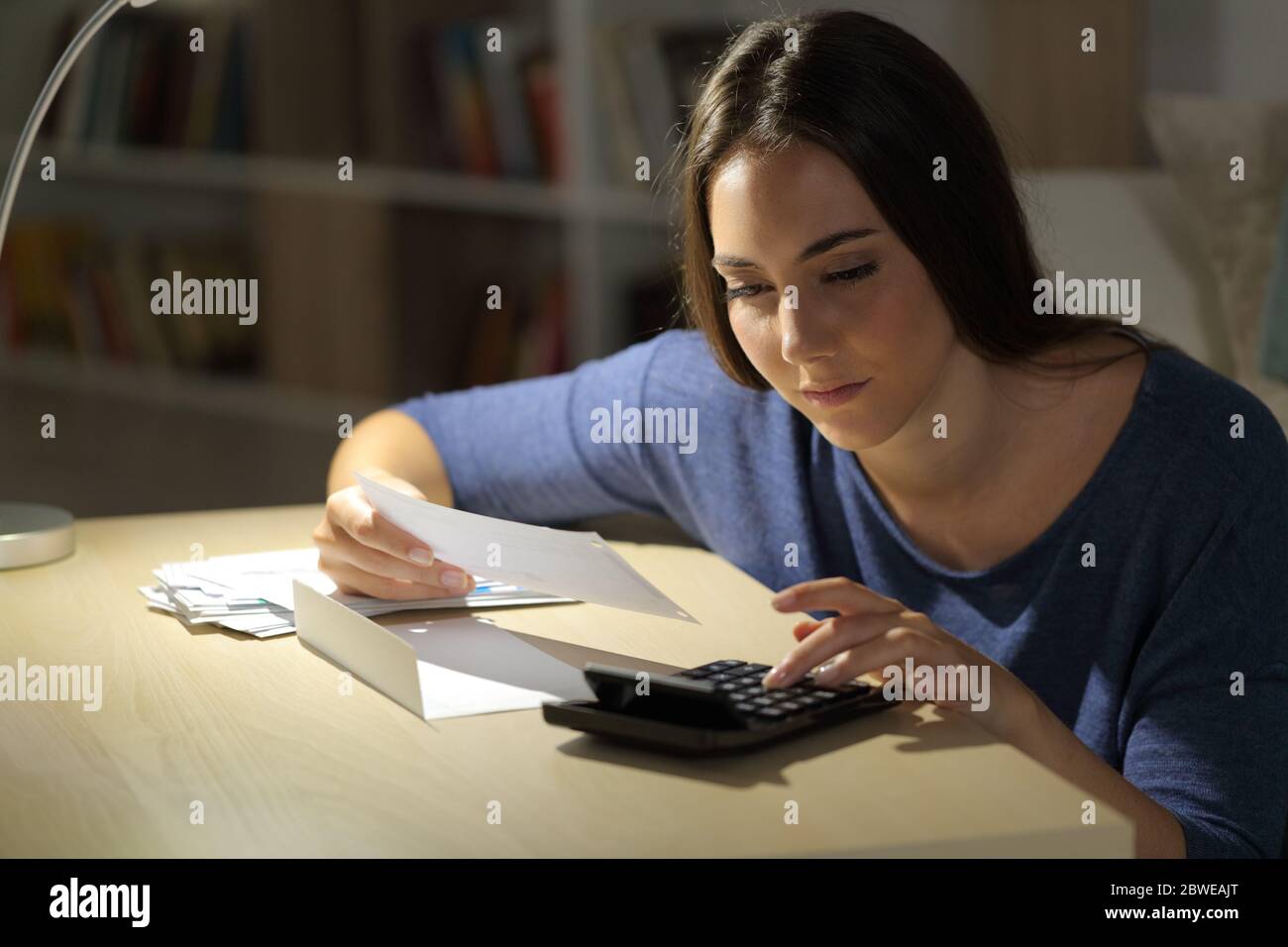 Femme sérieuse calculant les reçus sur la calculatrice assis sur une table la nuit à la maison Banque D'Images