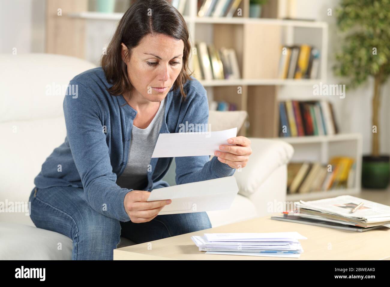Femme adulte sérieuse regardant les lettres de reçus assis sur le canapé à la maison Banque D'Images