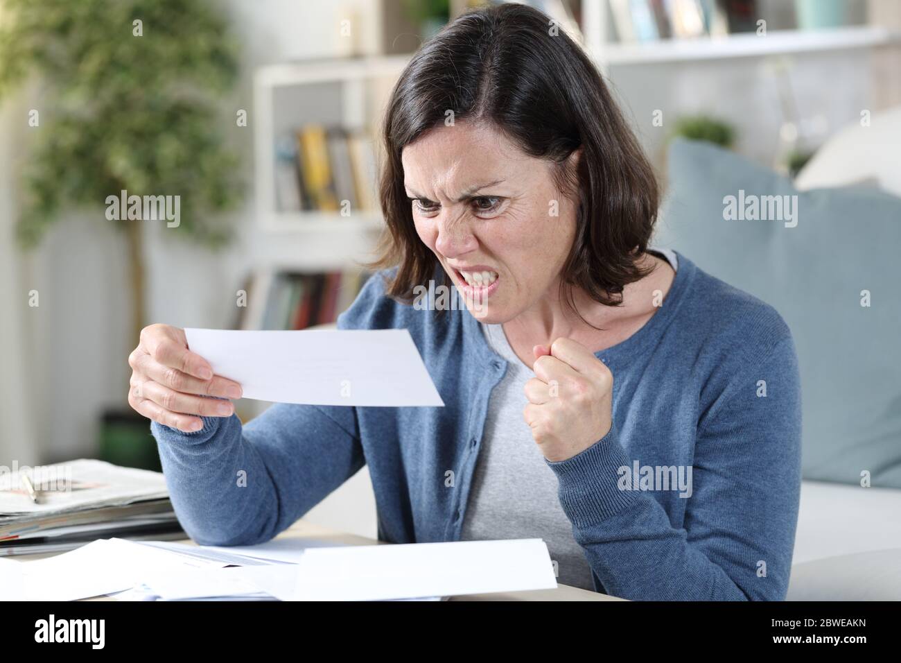 Femme adulte en colère regardant les reçus assis dans le salon à la maison Banque D'Images